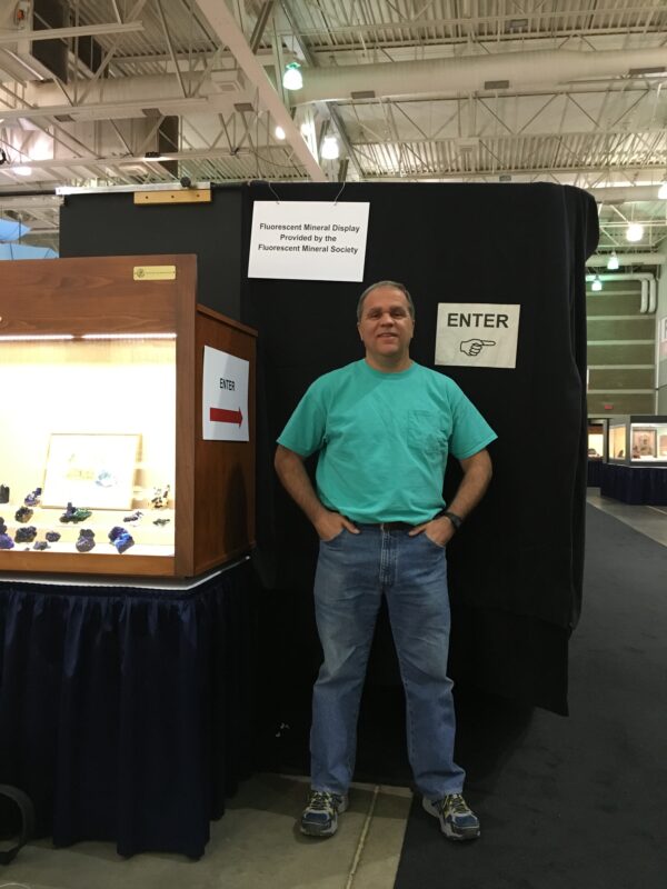 George Polman in front of the FMS display case.  Note the new length of black curtain and the new signs provided by the TGMS.  Photograph by Deborah S. Polman.